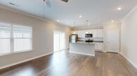 This single-story home is thoughtfully designed with a clean, modern aesthetic that flows seamlessly throughout. Rich hardwood-style flooring extends across the entire residence, complemented by crisp white trim, crown molding, and neutral wall tones that create a bright and cohesive atmosphere.

The open-concept living and kitchen area serves as the heart of the home. The kitchen is well-appointed with white shaker-style cabinetry, granite countertops, a subway tile backsplash, and stainless steel appliances including a refrigerator, range, and microwave. A large central island with an undermount sink and pendant lighting above provides ample workspace and casual seating potential. Sliding glass doors in the adjoining living area bring in natural light and offer outdoor access.

A wide hallway with a tray ceiling detail connects the living spaces to the private areas of the home. Bedrooms are generously proportioned, each featuring ceiling fans and closet space. One bedroom includes a walk-in closet with wire shelving systems offering organized storage.

The bathrooms are finished with white cabinetry, granite-topped vanities, and hardwood-style flooring. The primary bathroom features a dual-sink vanity, providing ample counter space. Overall, the home presents a polished, move-in-ready interior with consistent, quality finishes throughout.