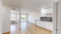 Located on East Lake Street in Minneapolis, MN, this efficiently designed one-bedroom, one-bathroom unit offers a clean, modern aesthetic throughout. Light hardwood flooring runs continuously across the entire space, complementing the crisp white walls and recessed lighting that give the interior a bright, airy feel.

The open-concept layout seamlessly connects the kitchen and living area. The kitchen is appointed with high-gloss white cabinetry extending to the ceiling, dark speckled countertops, a matching backsplash, and full appliances including a dishwasher, electric range, refrigerator, and microwave. A sliding glass door in the living area opens onto a private balcony, allowing natural light to fill the shared space and offering views of the surrounding Minneapolis neighborhood.

The bedroom is a comfortable, well-lit room featuring a large window with city views, a wall-mounted HVAC unit, and a built-in closet fitted with mirrored sliding doors that enhance the sense of space. The bathroom maintains the unit's modern design with light wood-look flooring, a full soaking tub with tiled marble-style surround, glass shelving, a vanity with integrated sink, and matte black hardware accents throughout. The overall ambiance is clean, contemporary, and move-in ready.