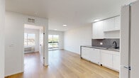 Located on East Lake Street in Minneapolis, MN, this efficiently designed one-bedroom, one-bathroom unit offers a clean, modern aesthetic throughout. Light hardwood flooring runs continuously across the entire space, complementing the crisp white walls and recessed lighting that give the interior a bright, airy feel.

The open-concept layout seamlessly connects the kitchen and living area. The kitchen is appointed with high-gloss white cabinetry extending to the ceiling, dark speckled countertops, a matching backsplash, and full appliances including a dishwasher, electric range, refrigerator, and microwave. A sliding glass door in the living area opens onto a private balcony, allowing natural light to fill the shared space and offering views of the surrounding Minneapolis neighborhood.

The bedroom is a comfortable, well-lit room featuring a large window with city views, a wall-mounted HVAC unit, and a built-in closet fitted with mirrored sliding doors that enhance the sense of space. The bathroom maintains the unit's modern design with light wood-look flooring, a full soaking tub with tiled marble-style surround, glass shelving, a vanity with integrated sink, and matte black hardware accents throughout. The overall ambiance is clean, contemporary, and move-in ready.