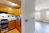 Located in Worcester, MA, this one-bedroom, one-bathroom residence offers a practical and comfortable layout across a single floor. The kitchen is efficiently designed with warm honey-toned wood cabinetry, granite-style countertops, a white subway tile backsplash accented with bold red and black tile details, tile flooring, and stainless steel appliances including a range and refrigerator. The kitchen flows into a combined dining area, making everyday living convenient and connected. The main living area features durable wood-style plank flooring in a cool gray tone, a ceiling fan with light fixture, baseboard heating, and large windows that invite generous natural light and views of surrounding greenery. The bedroom is a comfortable, well-proportioned room with the same wood-style flooring, a window with natural light, and baseboard heating. The bathroom is tiled in classic white subway tile with distinctive red and black accent squares, and includes a full bathtub and shower. Additional features include hallways connecting the spaces, a closet for storage, and a dedicated utility room. The neutral color palette and clean finishes throughout give the space a bright, move-in ready appeal.
