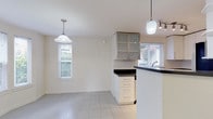 This single-floor residence offers a clean, bright interior defined by a neutral color palette and an efficient, well-organized layout. The kitchen is a functional centerpiece, featuring white cabinetry with sleek hardware, dark countertops, and a full suite of stainless steel appliances including a refrigerator, range, microwave, and dishwasher. Light tile flooring and a window with natural light make the space feel open and practical. A peninsula with a dark countertop separates the kitchen from an adjoining dining or flex area, which is accented by pendant and track lighting overhead and glass-front upper cabinetry for display. The living room is generously sized, finished with plush neutral carpet, and anchored by a fireplace with a wood-trimmed surround and mantle. Multiple windows invite natural light throughout, and a glass door opens to the exterior, enhancing the sense of connection to the outdoors. The bathroom is neatly finished with large-format tile flooring, a white vanity topped with a dark stone countertop, an undermount sink with modern hardware, and a combined tub and shower enclosed by sliding glass doors. Throughout the space, the consistently light walls and clean finishes contribute to a bright, move-in-ready ambiance.