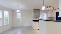 This single-floor residence offers a clean, bright interior defined by a neutral color palette and an efficient, well-organized layout. The kitchen is a functional centerpiece, featuring white cabinetry with sleek hardware, dark countertops, and a full suite of stainless steel appliances including a refrigerator, range, microwave, and dishwasher. Light tile flooring and a window with natural light make the space feel open and practical. A peninsula with a dark countertop separates the kitchen from an adjoining dining or flex area, which is accented by pendant and track lighting overhead and glass-front upper cabinetry for display. The living room is generously sized, finished with plush neutral carpet, and anchored by a fireplace with a wood-trimmed surround and mantle. Multiple windows invite natural light throughout, and a glass door opens to the exterior, enhancing the sense of connection to the outdoors. The bathroom is neatly finished with large-format tile flooring, a white vanity topped with a dark stone countertop, an undermount sink with modern hardware, and a combined tub and shower enclosed by sliding glass doors. Throughout the space, the consistently light walls and clean finishes contribute to a bright, move-in-ready ambiance.