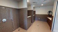 Located in Dallas, this single-floor facility is purpose-built for pet washing and grooming, offering a thoughtfully designed space that balances practicality with a clean, modern aesthetic. The interior is defined by richly toned dark brown subway tile that lines the walls to mid-height throughout, creating a durable and visually cohesive environment. Light-colored large-format floor tiles contrast the darker wall tile, contributing to a bright, hygienic feel underfoot.

Multiple open wash stations are arranged with low tiled partition walls, each equipped with chrome handheld shower fixtures and built-in ledges for storing grooming supplies. Floor drains are strategically positioned at each station to ensure efficient water management. Recessed lighting illuminates the space evenly throughout, while a ventilation system with ceiling-mounted HVAC vents maintains air quality and comfort.

The entry and transitional areas feature glass-paneled sliding doors that allow natural light to filter into the space from nearby windows, enhancing visibility and openness. A dispensing station is also present, providing convenient access to grooming products. Security cameras are installed throughout, ensuring a safe and monitored environment. Overall, the facility presents a clean, well-organized, and professional space designed for efficient and comfortable pet care.
