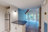 Located at 144 Larkin Way in South Burlington, Vermont, this two-floor residence offers 1 bedroom and 2 bathrooms across a well-designed layout. The main floor hosts the primary living areas, including an open-plan combined dining and living room distinguished by soaring vaulted ceilings, rich exposed wood beams, and a ceiling fan. Large windows frame lush green views, flooding the space with natural light and creating an airy, welcoming ambiance. Light wood-style flooring runs throughout the main living area. The galley-style kitchen is efficiently designed with cream shaker cabinetry, dark stone countertops, under-cabinet lighting, and stainless steel appliances, including a built-in microwave and range. A peninsula with matching countertop provides additional workspace. One full bathroom on this level features a tub/shower combo with tile surround and classic light tile flooring. Upstairs, the second floor offers a cozy carpeted bedroom bathed in natural light from a large skylight overhead, with angled ceilings following the roofline and the continued presence of warm wood beams. A second bathroom on this level features a clean walk-in shower with large-format white subway tile and built-in shelving. Two closets provide practical storage throughout the home.