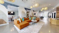 This thoughtfully designed amenity floor spans a generous footprint, offering residents a diverse range of communal spaces united by a cohesive contemporary aesthetic. The centerpiece is a large open lounge area featuring polished concrete floors, soaring ceilings, and striking globe pendant lights with woven, honeycomb-patterned shades that cast a warm, inviting glow. A bold abstract mural adorns the walls, complementing the rich caramel leather sectional sofa accented with teal and gold throw pillows. A wood-paneled media wall with a mounted flat-screen television adds warmth and texture to the seating area, while wicker accent chairs provide additional casual seating throughout.

A dedicated dining and coworking nook offers bar-height seating and a wall-mounted screen, ideal for both casual meals and productive work sessions. Glass-enclosed conference rooms provide private meeting spaces, furnished with round tables and upholstered chairs.

A game area features a shuffleboard table beneath an artistic industrial-style pendant light installation, adding a playful touch. The hallway connecting these spaces is lined with polished floors and decorative artwork, leading to dual elevators framed by warm wood-paneled walls.

The fitness center is well-appointed with cardio machines including treadmills, ellipticals, a rowing machine, and a stationary bike, alongside a comprehensive strength training station and a full dumbbell rack. Floor-to-ceiling mirrors and a large garage-style window overlooking the outdoors complete the bright, energizing workout environment.
