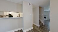 This two-story space is thoughtfully designed with a clean, neutral palette and updated finishes throughout. The main level centers around a welcoming living area highlighted by a white-mantled fireplace flanked by two windows that allow natural light to fill the room. Durable hardwood-style plank flooring runs throughout the first floor, complementing the light gray walls and crisp white baseboards. A pass-through opening connects the living area to the kitchen, which features gray shaker-style cabinetry, white quartz countertops, a stainless steel sink, and a bold navy blue subway tile backsplash. Stainless steel appliances, including a dishwasher, over-the-range microwave, and refrigerator, complete the kitchen. A carpeted staircase leads to the upper level, where bedrooms are finished with plush carpet and neutral walls, offering a comfortable and quiet retreat. A full bathroom on this level includes a tub-shower combo with white tile surround, gray vanity cabinetry, white countertops, and a modern mirror with contemporary lighting. An additional bathroom features a similar tub-shower configuration. The textured ceilings and consistent use of soft gray and white tones throughout give the space a cohesive, move-in ready appeal.