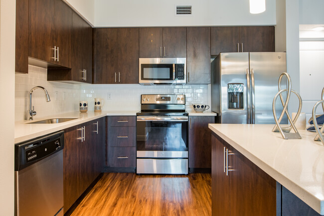 Kitchen with oak cabinetry, white countertops, white tile backsplash, and stainless steel appliances - Avalon Miramar