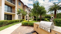This residence is located within a attractively designed Mediterranean-inspired community, characterized by warm stucco exteriors, arched architectural details, and multi-level buildings that frame beautifully maintained common grounds. The outdoor environment is a standout feature of the community, with manicured hedges, vibrant green lawns, mature shade trees, and neatly lined walkways with decorative brick paving that create an inviting, resort-like atmosphere. A built-in outdoor gas grill station is conveniently positioned along the paved common area, making it well-suited for outdoor gatherings and al fresco dining. Classic lamp post lighting is integrated throughout the grounds, adding both function and charm to the pedestrian pathways. Palm trees and tropical plantings reinforce the warm, Florida-inspired aesthetic of the community. The overall ambiance of the exterior setting is tranquil and well-appointed, reflecting thoughtful landscaping and community upkeep. Interior images were not sufficiently illuminated to provide detailed descriptions of the indoor spaces.