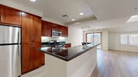 This two-story home offers a thoughtfully designed layout with distinct living spaces spread across both levels. The kitchen is a standout feature, showcasing rich cherry wood cabinetry, dark granite countertops, stainless steel appliances including a gas range and built-in microwave, and a generous peninsula that provides additional prep and seating space. Recessed lighting and a tray ceiling add definition to the kitchen area, which flows seamlessly into the main living space. The living area is finished with light hardwood-style flooring and benefits from soaring vaulted ceilings that create an airy, open atmosphere. A skylight and large windows invite abundant natural light throughout. Upstairs, a spacious bedroom features plush carpeting, a dramatic arched window, and vaulted ceilings that lend the room a grand, expansive feel. A full bathroom with tile flooring and a tub-shower combination completes the interior. Outside, a private patio area is enclosed by a wooden fence with a gated entry, offering seclusion beneath the shade of a mature tree. The surrounding grounds are well-maintained with lush landscaping, hedged walkways, and mature trees that create a peaceful, park-like setting.