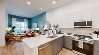 Located in Atlanta's Grant Park neighborhood, this single-floor residence at 1015 Boulevard SE presents a thoughtfully designed open-concept layout with contemporary finishes throughout. Light hardwood flooring flows seamlessly across the living, dining, and kitchen areas, creating a cohesive and airy feel.

The kitchen is a standout feature, showcasing two-tone cabinetry with gray lower cabinets and crisp white upper cabinets, both accented with gold hardware. White quartz countertops extend across a peninsula with bar seating, complemented by a white subway tile backsplash and a full suite of stainless steel appliances, including a gas range, built-in microwave, and French door refrigerator.

The open living area features a bold teal accent wall and large windows that invite abundant natural light and outdoor views. A dining nook with a round marble-top table sits adjacent to the kitchen.

The bedroom offers a serene retreat with soft sage-toned walls, large windows with views of the surrounding greenery, and direct access to an en-suite bathroom. The bathroom features gray cabinetry with matte black hardware, a white vanity, and a glass-enclosed walk-in shower with white tile surround and matte black fixtures.