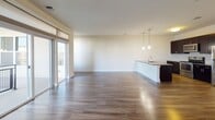 Located at 527 Old Bridge Tpke in East Brunswick, NJ, this single-floor residence offers a thoughtfully designed open-concept layout with modern finishes throughout. The spacious living area features rich hardwood flooring that extends seamlessly toward a sliding glass door opening to a private balcony, allowing natural light to fill the space. The contemporary kitchen is outfitted with dark espresso cabinetry, granite countertops, stainless steel appliances, and a breakfast bar with pendant lighting overhead — ideal for both everyday living and entertaining. A dedicated dining and kitchen corridor provides additional counter space and storage with matching cabinetry and a stainless steel sink. The bedroom is generously sized, finished with plush neutral carpeting and a large window that brings in ample natural light. The bathroom features classic white subway tile surrounding the bathtub, tile flooring, dark vanity cabinetry with granite countertops, and convenient in-unit stacked washer and dryer access. A carpeted hallway connects the main living areas to the bedroom and bathroom, with clean white panel doors and a neutral color palette that lends the entire space a bright, cohesive aesthetic.
