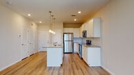 This well-appointed single-floor residence offers a thoughtfully designed open-concept layout that seamlessly connects the kitchen and living areas. The kitchen serves as the heart of the home, showcasing crisp white shaker-style cabinetry, light granite countertops, and a classic subway tile backsplash. A central island with an undermount sink and pendant lighting above provides additional workspace and a natural gathering point. Stainless steel appliances, including a refrigerator, range, and over-the-range microwave, complete the modern kitchen aesthetic. Light hardwood-style flooring flows throughout the main living areas, enhancing the bright and airy atmosphere. The living area benefits from large sliding glass doors that invite generous natural light and provide access to an outdoor area. Ceiling fans are present in both the living space and bedroom, contributing to comfort throughout. The bedroom is carpeted and features windows with blinds that allow for ample natural light. The en-suite bathroom is finished with a white vanity offering generous countertop space, a large mirror, and wood-style flooring. Directly accessible from the bathroom is a spacious walk-in closet equipped with wire shelving and hanging rods, offering abundant storage. Recessed lighting throughout the main areas adds to the clean, contemporary feel of this well-designed space.