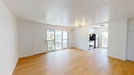 This 550-square-foot, one-bedroom, one-bathroom apartment is located at 2131 N Cahuenga Blvd, Unit 27, in the heart of Los Angeles, CA. The unit is thoughtfully laid out across a single floor, encompassing a living room, bedroom, kitchen, bathroom, and hallway. Light wood flooring runs throughout, creating a warm and cohesive aesthetic. The living room is bright and open, featuring a modern multi-bulb chandelier, a wall-mounted A/C unit, and large sliding glass doors that provide direct outdoor access and ample natural light. The galley-style kitchen is well-appointed with white shaker cabinets, subway tile backsplash, stainless steel appliances including a gas range, microwave, refrigerator, and dishwasher, along with a dual-basin sink and a window overlooking the exterior. The 140-square-foot bedroom offers a ceiling fan, natural light from dual windows, and a built-in closet with sliding doors and upper cabinetry for generous storage. The bathroom is clean and modern, featuring a white vanity, tiled shower-tub combo, and matte black fixtures, accented by a frosted window for natural light and privacy. Built-in hallway storage cabinetry adds further practicality to this efficiently designed urban apartment.