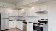 This single-floor unit presents a clean, modern design characterized by light hardwood-style flooring and crisp white walls throughout. The kitchen serves as a standout feature, showcasing white shaker-style cabinetry with brushed nickel hardware, dark granite countertops, and a white subway tile backsplash. Stainless steel appliances — including a range, dishwasher, and range hood — are integrated seamlessly into the layout, which offers generous counter and cabinet space arranged in an L-shape configuration. Recessed lighting illuminates the kitchen, complementing the open sightline into the living area.

The living space is open and airy, with light-toned flooring extending throughout and neutral walls that allow for flexible styling. Bedroom areas are well-proportioned, with one featuring a large window that brings in natural light and views of the surrounding brick exterior. A closet with bifold doors provides practical storage. The hallway is bright and efficiently laid out, with a wall-mounted thermostat and flush ceiling lighting.

The bathroom is finished with large-format marble-look tile on both the floor and tub surround, a white vanity with a solid countertop, and a window that introduces natural light, creating a clean, spa-like atmosphere.