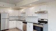 This single-floor unit presents a clean, modern design characterized by light hardwood-style flooring and crisp white walls throughout. The kitchen serves as a standout feature, showcasing white shaker-style cabinetry with brushed nickel hardware, dark granite countertops, and a white subway tile backsplash. Stainless steel appliances — including a range, dishwasher, and range hood — are integrated seamlessly into the layout, which offers generous counter and cabinet space arranged in an L-shape configuration. Recessed lighting illuminates the kitchen, complementing the open sightline into the living area.

The living space is open and airy, with light-toned flooring extending throughout and neutral walls that allow for flexible styling. Bedroom areas are well-proportioned, with one featuring a large window that brings in natural light and views of the surrounding brick exterior. A closet with bifold doors provides practical storage. The hallway is bright and efficiently laid out, with a wall-mounted thermostat and flush ceiling lighting.

The bathroom is finished with large-format marble-look tile on both the floor and tub surround, a white vanity with a solid countertop, and a window that introduces natural light, creating a clean, spa-like atmosphere.