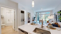 Located at 100 Pine St W in Wilson, NC, this one-bedroom, one-bathroom unit offers a thoughtfully designed open-concept layout that maximizes its efficient footprint. The kitchen is a standout feature, showcasing white shaker cabinetry, a subway tile backsplash, quartz countertops, and a full suite of stainless steel appliances including a refrigerator, range, and over-the-range microwave. A kitchen island with an undermount sink provides additional prep space and flows seamlessly into the bright living area. The living room is bathed in natural light from large windows and a glass door that opens to a private balcony with outdoor views, creating a welcoming and airy atmosphere. Light wood-style flooring runs throughout the main living areas, complementing the neutral, modern aesthetic. The bedroom is a comfortable retreat featuring plush carpet, a ceiling fan, a window with exterior views, and direct access to a dedicated closet. A stacked washer and dryer unit is conveniently tucked within the unit. The bathroom features a white vanity with an undermount sink, a round mirror, and a combination tub and shower. Clean white walls and consistent finishes throughout give the entire space a cohesive, contemporary feel.