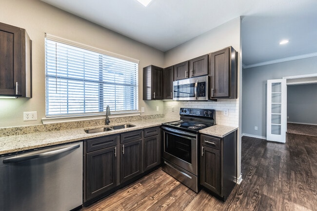 Kitchen with espresso cabinetry, speckled granite countertops, white subway tile backsplash, stainless steel appliances, and hard surface flooring - eaves North Dallas