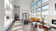 Located at 5875 Balsam Dr in Hudsonville, Michigan, this single-floor community clubhouse offers a well-appointed gathering space defined by striking architectural design and an open, airy atmosphere. Soaring vaulted and double-height ceilings amplify the sense of spaciousness throughout, while expansive floor-to-ceiling windows and clerestory glazing flood the interiors with abundant natural light and frame views of the surrounding landscape.

The main lounge area is anchored by a sleek linear fireplace with a wall-mounted television above, providing an inviting focal point for relaxed conversation. Mid-century modern furnishings — including a caramel leather sofa, wood-framed armchairs, and patterned area rugs — lend warmth and style to the space. A sunlit dining zone features bistro-height tables and leather barstools, with large glass sliding doors opening directly to an outdoor patio area.

The kitchen is equipped with crisp white shaker cabinetry, granite countertops, a large island with seating, stainless steel appliances, and hardwood flooring — making it well-suited for events and gatherings. Throughout the space, white walls, bold black window frames, and natural wood accents create a cohesive modern aesthetic. Direct exterior access via double glass doors further connects the interior to the outdoors.