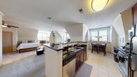 Located at 2501 9th Rd S in Arlington, Virginia, this efficiently designed single-floor unit offers a thoughtfully arranged open-concept layout that maximizes every square foot. The kitchen is well-appointed with rich dark-wood cabinetry, dark granite countertops, stainless steel appliances including a refrigerator, range, microwave, and dishwasher, and a peninsula with bar seating that serves as a natural divider between the kitchen and living areas. Light-toned tile flooring runs throughout the kitchen, transitioning seamlessly to plush carpeting in the living and sleeping zones. The dining area is tucked into a bright alcove framed by angled architectural walls and a large window that invites natural light, creating an intimate yet open setting. The living area features vaulted, angled ceilings that add visual interest and a sense of spaciousness, complemented by multiple windows with blinds offering exterior views. The full bathroom includes a single-sink vanity with white countertop, warm wood cabinetry, and dual mirrors. Crown molding and consistent neutral tones throughout lend the space a cohesive, polished aesthetic. The open floor plan and architectural angles make this a distinctive and functional residence in the heart of Arlington.