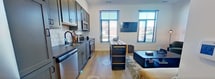 This 470 square foot apartment in Newport News, VA, maximizes its compact footprint with a thoughtful open-concept design. The main living area combines the kitchen, dining, and living spaces seamlessly. The kitchen boasts gray cabinetry, stainless steel appliances, and a subway tile backsplash, with a small island providing additional counter space and storage.

The living room features comfortable seating, including two plush armchairs and a sofa, centered around a sleek coffee table. Large windows flood the space with natural light, while modern lighting fixtures and artwork add character. Light wood flooring throughout creates a sense of continuity and warmth.

The bedroom, measuring 100 square feet, is efficiently designed with a queen-sized bed, nightstands, and built-in closet space. Neutral tones and subtle decor maintain a calm atmosphere. The bathroom showcases a tiled shower/tub combination, a modern vanity, and coordinating towels and bath mat.

Despite its modest size, the apartment doesn't compromise on style or functionality. Clever storage solutions and a cohesive color palette contribute to a spacious feel, making this one-bedroom apartment an ideal urban dwelling for those seeking a contemporary living space.