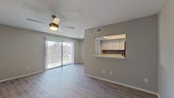 This well-appointed one-bedroom, one-bathroom unit offers a thoughtfully designed single-floor layout that maximizes functionality and comfort. The living area features wood-look plank flooring, neutral gray walls, and a ceiling fan with integrated lighting. A sliding glass door lined with vertical blinds opens to a private balcony, allowing natural light to fill the space and offering pleasant outdoor views of surrounding greenery.

The kitchen is connected to the living area via a pass-through window with a breakfast bar overhang, creating an open and interactive feel. Inside, the kitchen is equipped with white upper cabinets, dark lower cabinetry, light countertops, a mosaic tile backsplash, and black appliances including a range, microwave, dishwasher, and refrigerator. A tray ceiling detail adds an architectural touch overhead.

The bedroom is a comfortable size, finished with plush gray carpeting, a window with blinds for natural light, and access to a spacious walk-in closet featuring carpet flooring and built-in hanging rods. The bathroom includes a full tub-shower combo with white tile surround and chrome fixtures. Textured ceilings are present throughout, lending a consistent finish to the overall aesthetic of this practical and move-in-ready home.