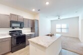 This single-floor unit presents a well-organized, open-concept layout that seamlessly connects the kitchen and living areas. The kitchen is a functional centerpiece, anchored by a central island with a light granite-style countertop and an integrated sink. Dark taupe cabinetry lines the walls, providing ample storage, while light wood-look flooring ties the space together. Black appliances, including a gas range, over-the-range microwave, and refrigerator, complete the kitchen's practical design.

The kitchen flows directly into the living area, which features light carpet, recessed lighting, and a ceiling fan. A window with blinds allows natural light to brighten the space, creating an inviting and airy atmosphere.

The bedroom is a calm, carpeted retreat with neutral walls, a ceiling fan, and a window overlooking greenery, offering a quiet, comfortable environment.

The bathroom is cleanly designed with wood-look tile flooring, a single-sink vanity topped with a granite-style surface, a large mirror with overhead lighting, and a full tub-shower combination. The overall aesthetic throughout the unit is consistent—neutral tones, modern fixtures, and practical finishes that create a cohesive, move-in-ready living space.