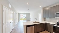 This single-floor, 3-bedroom, 3-bathroom residence offers a thoughtfully designed layout that balances modern aesthetics with everyday functionality. The open-concept kitchen and living area serves as the heart of the home, featuring sleek dark wood cabinetry, stainless steel appliances including a refrigerator, range, and microwave, light subway tile backsplash, and a large kitchen island with an undermount sink and ample counter space. Light hardwood flooring flows through the main living areas, while large sliding glass doors flood the living room with natural light and provide outdoor views.

The primary bedroom is a well-sized retreat with hardwood-style flooring, multiple closet access points, and a dedicated en-suite bathroom. The primary bath is outfitted with a dual-sink vanity featuring dark cabinetry, quartz countertops, large mirrors, and a glass-enclosed walk-in shower with a window for natural light. The two additional bedrooms offer soft carpet flooring, ceiling fans, and multiple windows that bring in abundant natural light. A dedicated closet provides additional storage. The neutral color palette of warm grays and whites throughout creates a clean, cohesive ambiance across the entire residence.