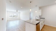 This well-appointed 2-bedroom, 2-bathroom residence is designed with a clean, modern aesthetic and thoughtful layout across a single floor. The open-concept kitchen and living area forms the heart of the home, where a granite-topped island with a stainless steel sink anchors the space. Pendant lighting illuminates the island, while white shaker cabinetry and a full suite of stainless steel appliances — including a range, microwave, refrigerator, and dishwasher — complete the kitchen. Light wood-style flooring flows seamlessly throughout the home, complementing the crisp white walls and adding warmth to every room. The living area is bright and airy, benefiting from a large window and a ceiling fan overhead. The primary bedroom offers a comfortable footprint with natural light streaming through wide, blinds-fitted windows and direct access to a hallway leading to a bathroom. The en-suite bathroom features a walk-in glass shower, granite vanity countertop, and white cabinetry. The second bathroom is equally well-finished, with a full soaking tub, granite vanity, and consistent modern detailing. Three closets provide ample storage throughout. The overall ambiance is bright, clean, and move-in ready.