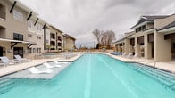 This single-floor amenity facility serves a multi-building residential community and is thoughtfully designed to support everyday living with a range of shared conveniences. At the heart of the outdoor area is a generously sized resort-style swimming pool with crystal-clear turquoise water, flanked by rows of lounge chairs and in-pool sun shelf seating. The pool is framed by multi-story residential buildings with covered balconies, creating a well-defined and welcoming courtyard atmosphere. A dedicated pool house structure nearby adds additional functionality to the outdoor space.

Inside, the communal laundry facility is expansive and practical, featuring high ceilings with exposed steel beams and industrial-style lighting that lend the space a clean, utilitarian character. Polished concrete floors run throughout, and a full lineup of commercial-grade washing machines and dryers lines the walls, offering ample capacity for residents. A long countertop provides a convenient folding surface, and natural light filters in through windows near the entrance door.

Adjacent to the laundry area is a waiting lounge with the same concrete flooring and exposed overhead infrastructure. The space includes a built-in counter ledge and seating, providing a functional area for residents to wait comfortably while completing their laundry.