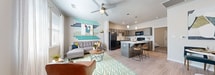 This thoughtfully designed single-floor unit offers a seamless open-concept layout connecting the living area and kitchen. The living room features light wood-style flooring, a ceiling fan, large windows that invite natural light, and a vibrant accent wall adorned with colorful horizontal wall art that adds a contemporary, artistic touch to the space.

The kitchen is a functional centerpiece, equipped with rich gray-toned cabinetry, light countertops, and black appliances including a refrigerator, stove, microwave, and dishwasher. A peninsula island with bar seating and stylish pendant lighting above serves as both a prep area and casual dining space, creating a natural transition between the kitchen and living areas.

The bedroom is a comfortable retreat featuring a ceiling fan, windows with natural light, and warm, neutral tones that contribute to a relaxed ambiance. The full bathroom is well-appointed with dark wood cabinetry, a large vanity mirror, and light flooring that complements the overall aesthetic of the unit.

A dedicated in-unit laundry room provides added convenience, complete with a full-size washer and dryer, built-in shelving, and additional storage space. Light wood-style flooring flows consistently throughout the unit, unifying the space with a clean, modern feel.
