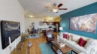 This single-floor residence offers a thoughtfully designed open-concept layout that seamlessly connects the living, dining, and kitchen areas. The living room is a standout space, anchored by a bold teal accent wall, warm hardwood-style flooring, and a ceiling fan overhead. Natural light filters in through large windows dressed with sheer curtains, creating a bright and welcoming atmosphere. The kitchen is well-equipped with dark espresso cabinetry, granite-style countertops, stainless steel appliances, pendant lighting over a center island, and a dedicated wine rack — ideal for both everyday cooking and entertaining. The adjacent dining area provides a comfortable space for meals and connects conveniently to an in-unit laundry room. Both bedrooms are generously sized, featuring plush carpeting, ceiling fans, and large windows that bring in natural light. Each bedroom is complemented by its own teal accent wall, adding a consistent design thread throughout the home. The two bathrooms mirror each other in finish, offering dark-toned vanities with granite countertops, hardwood-style flooring, and tub-shower combinations. Together, the spaces deliver a cohesive, modern aesthetic with practical, everyday functionality.