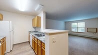 Located on Douglas Avenue in Racine, Wisconsin, this one-bedroom, one-bathroom residence offers a practical and comfortable layout across a single floor. The open-concept kitchen and living area serves as the heart of the home, where a peninsula with a double stainless steel sink and granite-look countertops separates the kitchen from the living space. Warm oak cabinetry provides ample storage, complemented by white appliances including a range, microwave, and dishwasher. Light hardwood-style flooring runs through the kitchen, transitioning to plush carpeting in the living area, which benefits from natural light through a window. The generously sized bedroom features soft carpeting, a ceiling fan with light fixture, a window overlooking the greenery outside, and a sliding-door closet offering substantial storage. A second closet provides additional organization options. The full bathroom is well-finished with an oak vanity, a large mirror, a lighted vanity bar, and a step-in tub and shower combination equipped with grab bars. Neutral wall tones and consistent warm wood accents throughout create a cohesive, inviting atmosphere.