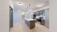 This single-floor, 3-bedroom, 2-bathroom unit offers a well-designed open-concept layout that maximizes its functional living space. The kitchen and living room share a seamlessly connected footprint, anchored by a striking central island with a marble-style countertop and an integrated sink. Pendant lighting hangs above the island, complementing the dark espresso cabinetry, white subway tile backsplash, and a full suite of stainless steel appliances including a refrigerator, range, and built-in microwave. The adjacent living area features light wood-style flooring, a ceiling fan with light fixture, and access to an outdoor space through a glass-paneled door, allowing natural light to fill the room.

The three bedrooms are finished with plush carpeting and neutral-toned walls, providing a comfortable retreat. The two bathrooms are outfitted with dark wood vanities, matching hardware, and a tub-shower combination. A dedicated in-unit laundry room houses a full-size washer and dryer, adding everyday convenience. A hallway connects the bedroom wing to the main living areas, and a closet provides additional storage. Light wood-style flooring runs consistently through the non-carpeted areas, tying the unit's modern aesthetic together cohesively.