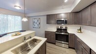 Located at 1608 East South Riverton Avenue in Spokane, WA, this single-floor unit offers a well-designed layout with contemporary finishes throughout. The kitchen is a standout feature, showcasing rich dark-toned shaker-style cabinetry paired with white quartz countertops, stainless steel appliances including a refrigerator, range, and microwave, and a large undermount sink set into a peninsula. Track lighting and pendant fixtures illuminate the space, which flows seamlessly onto wood-look plank flooring that extends through the main living areas. The living room is bright and welcoming, with a glazed exterior door and a large window that invite natural light and provide outdoor access. Two well-proportioned bedrooms feature plush carpeting, large windows, and ample wall space. The primary bedroom includes direct access to additional rooms, adding functional versatility. Two full bathrooms are finished with wood-look flooring, dark vanity cabinetry, and white countertops. One bathroom offers a soaking tub and shower combination, while the second features a walk-in shower. Clean white walls and consistent modern hardware tie the entire space together, creating a cohesive and comfortable living environment.