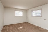 This single-floor unit offers a straightforward, functional layout with a clean, neutral aesthetic throughout. The living area is carpeted in warm beige tones and connects openly to the kitchen, which is separated by a half-wall peninsula that doubles as a breakfast bar. The kitchen is equipped with warm-toned wooden cabinetry extending to the upper walls for ample storage, a gas range, and a full-size refrigerator. Tile flooring in the kitchen provides a practical transition from the carpeted living space. A ceiling fan with a light fixture keeps the area well-ventilated and lit.

The bedrooms are generously proportioned, each featuring wall-to-wall beige carpeting and bright white walls. Multiple windows fitted with horizontal blinds allow natural light to fill the rooms, creating an airy atmosphere. Electrical outlets are conveniently placed throughout.

The bathroom is finished with white tile surrounding the full-size bathtub and shower combination, complete with a handheld showerhead and a shower curtain rod. A tile floor adds durability to the space. The overall design of the unit is practical and clean, offering a comfortable, move-in-ready environment.