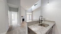 This thoughtfully designed one-bedroom, one-bathroom residence offers an efficient and comfortable layout across a single floor. The open-concept kitchen and living area serves as the heart of the home, highlighted by dramatic vaulted ceilings that lend a sense of spaciousness well beyond the unit's footprint. The kitchen features dark espresso cabinetry, granite countertops, a peninsula with a pull-down faucet, stainless steel appliances including a refrigerator, range, and microwave, and stylish pendant lighting overhead. Light wood-look flooring grounds the kitchen, which flows seamlessly into the carpeted living area. The living room centers around a fireplace with a wood mantel and granite hearth, flanked by soaring walls and French doors that open to a private balcony overlooking a landscaped green area. The spacious primary bedroom includes plush carpeting, a ceiling fan, and access to two closets. The bathroom is finished with tile-surround tub/shower, a dark vanity with granite countertop, and wood-look flooring. A dedicated laundry room houses a full-size washer and dryer alongside the water heater. Two hallways connect the home's rooms efficiently, completing a functional and attractive layout.