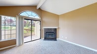 This single-story home in Pittsburg, CA (94565) offers a well-designed open layout with notable architectural details throughout. The living room is an immediate highlight, featuring soaring vaulted ceilings with exposed beam accents and a striking arched transom window that floods the space with natural light. A dark granite-surround fireplace with a white mantel serves as a focal point, while sliding glass doors open directly onto an outdoor deck with views of landscaped surroundings and mature trees. Plush wall-to-wall carpeting adds warmth to the living area.

The kitchen is outfitted with warm honey-toned wood cabinetry, dark granite countertops, and a full suite of black appliances including a refrigerator, gas range, microwave, and dishwasher. Wood-look flooring runs throughout the kitchen, which connects seamlessly to the main living space via an open pass-through layout beneath a vaulted ceiling with a ceiling fan and pendant light.

The bedroom is a calm, well-proportioned room with carpet flooring and a large grid-pane window offering garden views. The bathroom features wood-look flooring, a granite-topped vanity with wood cabinetry, and a tub/shower combination. A dedicated in-unit laundry closet houses a full-size washer and dryer, adding everyday convenience.