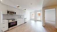 Located on Santa Monica Boulevard in the heart of West Los Angeles, this 2-bedroom, 1-bathroom unit offers a clean, modern aesthetic defined by a neutral palette and light wood-style flooring that runs throughout the entire space. The open-concept layout connects the kitchen and living area seamlessly, creating an efficient and welcoming flow. The kitchen is well-appointed with flat-front light gray cabinetry, a full suite of stainless steel appliances including a refrigerator, range, microwave, and dishwasher, a tile backsplash, and gold-accented fixtures that add a contemporary touch. Directional sconce lighting highlights the kitchen area with a stylish, modern flair. The living area is bright and airy, benefiting from a glass door that opens to a private balcony with outdoor views. Both bedrooms are finished in the same light tones, with the primary bedroom featuring a dedicated walk-in closet with built-in shelving, and the second bedroom offering a sliding door closet. Natural light filters in through well-placed windows, enhancing the open feel of each room. The bathroom features warm wood-toned cabinetry, a white countertop vanity with an arched mirror, and accessibility grab bars. A hallway connects all rooms, completing this thoughtfully designed, move-in-ready unit.