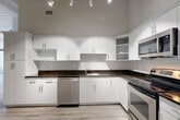 Located at 24 Mt Vernon St in Lynn, Massachusetts, this 1-bedroom, 1-bathroom residence offers a thoughtfully designed single-floor layout with modern finishes throughout. The space is defined by soaring ceilings with exposed structural beams and track lighting that illuminate the open-concept interior, creating an airy, loft-like atmosphere.

The kitchen is a standout feature, showcasing sleek white flat-panel cabinetry that extends to the ceiling, providing generous storage. Dark granite countertops contrast sharply with the white cabinetry, while a full suite of stainless steel appliances — including a refrigerator, electric range, over-the-range microwave, and dishwasher — adds a polished, contemporary look. Light wood-style flooring runs throughout the main living areas, enhancing the brightness of the space.

The bathroom is finished with large-format dark slate tile flooring, a white vanity with drawer storage, and clean white walls, creating a crisp and functional environment. A dedicated closet provides practical storage solutions.

Natural light enters through windows visible from the main living area, complemented by the industrial-style track lighting overhead. A barn-style sliding door adds a distinctive architectural accent, reinforcing the modern-industrial character of this well-designed Lynn residence.