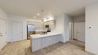 Located at 15922 E Valleyway Ave in Spokane, Washington, this thoughtfully designed single-floor residence offers a clean, contemporary aesthetic throughout. The open-concept kitchen serves as the heart of the unit, showcasing light wood-toned cabinetry extending to the ceiling, crisp white countertops, and a large peninsula with an integrated sink — ideal for both meal preparation and casual dining. Stainless steel appliances, including a side-by-side refrigerator, electric range, and built-in microwave, complete the well-appointed kitchen. Stylish pendant lights hang above the peninsula, adding a modern touch, while recessed lighting illuminates the space further. Light-toned hardwood-style flooring flows through the main living areas, lending warmth and continuity. The living area features a large window and private door access, allowing natural light and outdoor views of the surrounding greenery. Bedrooms are finished with plush carpet, neutral walls, and windows that bring in natural light. At least one bedroom includes access to a walk-in closet with built-in shelving, offering generous storage. The overall palette of soft whites, warm wood tones, and neutral finishes creates a bright, cohesive, and move-in-ready living environment.