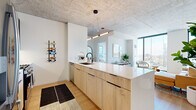Located in Chicago's dynamic West Loop neighborhood, this modern residence at 160 N Morgan St blends industrial-chic architecture with contemporary finishes to create a refined urban living experience. Exposed concrete ceilings throughout lend an authentic loft-like character, while light hardwood flooring and crisp white walls provide a clean, airy contrast.

The open-concept kitchen is a standout feature, showcasing a generous waterfall-edge island with warm natural wood cabinetry, a matte black faucet, and pendant lighting that draws the eye. Upper cabinetry in deep charcoal frames stainless steel appliances, completing a polished, functional design. The kitchen flows seamlessly into the living area, where expansive floor-to-ceiling windows frame sweeping Chicago skyline views, flooding the space with natural light.

The bedrooms continue the theme of light-filled, modern living, each benefiting from large-format windows overlooking the city. The primary bathroom features large-format tile, a glass-enclosed walk-in shower with a terrazzo floor, and matte black hardware accents. A secondary bathroom includes tile flooring and built-in shelving. Throughout the residence, the interplay of industrial elements and contemporary design creates a sophisticated, cohesive ambiance ideal for urban living.