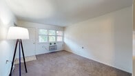 This single-floor unit offers a straightforward, efficient layout designed for comfortable everyday living. The main living area is generously proportioned, featuring neutral-toned carpeting, crisp white walls, and a wall-mounted HVAC unit positioned beneath a set of windows that draw in natural light and offer views of surrounding greenery. A closet and entry door are conveniently located within the living space, contributing to its functional design. Baseboard heating runs along the perimeter, providing an additional climate control option.

The kitchenette is thoughtfully arranged, featuring warm oak cabinetry both above and below the counter, a stainless steel sink, granite-style laminate countertops, and a full-size refrigerator in a sleek dark finish. Tile flooring runs through this area, providing a practical and easy-to-maintain surface.

The bathroom is clean and well-appointed, with a tub-shower combination enclosed by a decorative curtain, a toilet, and a wood-framed vanity mirror above a single-sink vanity with oak cabinetry. Tile flooring completes the space with a cohesive finish.

Overall, the unit presents a clean, neutral palette throughout, making it a versatile and move-in-ready space.