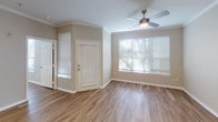 This single-floor residence presents a clean, contemporary interior designed for comfortable everyday living. The kitchen is outfitted with white shaker-style cabinetry, light quartz countertops, a subway tile backsplash, stainless steel appliances including a double oven range and built-in microwave, and a double-basin undermount sink with a gooseneck faucet. A peninsula counter extends into the living area, creating a natural transition between the two spaces.

The open living area features warm wood-look flooring that extends throughout the unit, crown molding accents, and a ceiling fan with integrated lighting. A large window allows natural light to fill the space, offering views of surrounding greenery. The layout flows directly from the entry toward the kitchen and living zones, creating an efficient, connected floor plan.

The bedrooms are well-proportioned, each featuring ceiling fans, wood-look flooring, and windows with exterior views. One bedroom includes access to a private bathroom with a vanity, mirror, and a full tub-shower combination with white tile surround, as well as an adjacent walk-in closet. The neutral color palette of soft greiges and whites is consistent throughout, contributing to a cohesive and light-filled ambiance across the entire space.
