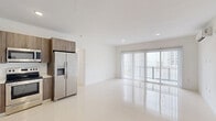 Located at 25850 SW 140th Court in Homestead, Florida, this four-bedroom, two-bathroom unit offers a clean, modern design across a single floor. The layout is efficiently organized, connecting a central hallway to all four bedrooms, each finished with bright white walls, polished large-format tile floors, and individual closets — including walk-in options — fitted with wire shelving systems. The kitchen features full-height wood-tone cabinetry, light countertops, a stainless steel dishwasher, range, microwave, and a French door refrigerator, all set against a crisp white backdrop with recessed lighting overhead. An open adjacent area provides flexible living or dining space. Both bathrooms are appointed with marble-style wall surrounds in the walk-in showers, modern floating vanities with wood-tone cabinetry, white countertops, and polished tile flooring, lending a sleek, contemporary feel. The primary bedroom offers a comfortable footprint with its own closet. Sliding glass doors in one of the bedrooms invite natural light and provide views of the surrounding community. The overall aesthetic is clean and minimalist, with a consistent neutral palette and modern finishes throughout.