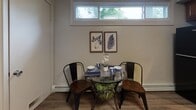 This single-floor unit offers a thoughtfully arranged layout visible across multiple distinct living spaces. The kitchen stands out with rich warm-toned cabinetry, granite countertops, a white subway tile backsplash, and black appliances including a gas range, built-in microwave, and dishwasher. Recessed lighting and wood-look flooring complete the polished look.

A cozy dining nook adjacent to the kitchen features a wide transom window that draws in natural light, creating an airy atmosphere ideal for casual meals. The living area connects fluidly to the rest of the unit, anchored by wood-look flooring and neutral walls.

The unit includes multiple bedrooms, each carpeted and fitted with vertical blinds over windows that allow natural light. One bedroom features a mirrored sliding closet and a built-in baseboard heater, while another is styled in cool blue tones with multiple windows. A third bedroom showcases a brick-accent wall and garden views.

A full bathroom offers tiled walls, a shower-tub combination, pedestal sink, and wood-look flooring. A separate flexible room with carpet and a window serves well as a home office or den, completing this versatile and well-lit space.