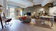 This two-bedroom, two-bathroom residence showcases a distinctly Detroit-inspired aesthetic, blending urban character with thoughtful design across a single-floor open layout. The living area commands attention with a dramatic floor-to-ceiling floral wallpapered accent wall, complete with a bold "DETROIT" marquee sign, mounted television, and exposed ductwork that adds an industrial edge. Wide-plank hardwood-style flooring, generous natural light from large glass doors, and an airy ceiling height contribute to a welcoming, open feel throughout.

The kitchen is well-appointed with stainless steel appliances, a mosaic tile backsplash, white upper cabinetry with open shelving, and a granite-topped island with bar seating—ideal for both cooking and casual dining. Pendant lighting adds warmth overhead.

The primary bedroom features a striking black-and-white Detroit cityscape mural spanning the full accent wall, creating a dramatic focal point behind the bed. The en-suite bathroom offers a vanity with granite countertops, herringbone-patterned tile flooring, bold red-toned walls, and a glass-enclosed shower. The second bathroom mirrors the quality finishes with a tub-shower combination and vivid blue striped walls, continuing the residence's expressive design theme throughout.