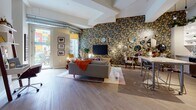 This two-bedroom, two-bathroom residence showcases a distinctly Detroit-inspired aesthetic, blending urban character with thoughtful design across a single-floor open layout. The living area commands attention with a dramatic floor-to-ceiling floral wallpapered accent wall, complete with a bold "DETROIT" marquee sign, mounted television, and exposed ductwork that adds an industrial edge. Wide-plank hardwood-style flooring, generous natural light from large glass doors, and an airy ceiling height contribute to a welcoming, open feel throughout.

The kitchen is well-appointed with stainless steel appliances, a mosaic tile backsplash, white upper cabinetry with open shelving, and a granite-topped island with bar seating—ideal for both cooking and casual dining. Pendant lighting adds warmth overhead.

The primary bedroom features a striking black-and-white Detroit cityscape mural spanning the full accent wall, creating a dramatic focal point behind the bed. The en-suite bathroom offers a vanity with granite countertops, herringbone-patterned tile flooring, bold red-toned walls, and a glass-enclosed shower. The second bathroom mirrors the quality finishes with a tub-shower combination and vivid blue striped walls, continuing the residence's expressive design theme throughout.