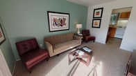 This two-floor, 2-bedroom, 1-bathroom residence offers a well-organized and functional layout designed for comfortable everyday living. The living room serves as the heart of the home, featuring soft teal accent walls, plush carpeting, and a sliding glass door that fills the space with natural light while providing direct access to an outdoor area. The room comfortably accommodates a seating arrangement and entertainment setup, creating an inviting atmosphere. The kitchen is thoughtfully designed with warm oak cabinetry, light countertops, and tile flooring. It includes a full suite of white appliances — a range, dishwasher, and refrigerator — along with a window that brings in natural light. A compact dining area adjacent to the kitchen provides a convenient space for everyday meals. Both bedrooms feature soft carpeting and windows that allow natural light to brighten each room. The primary bedroom offers ample space, while the second bedroom provides flexibility for guests or a home office. The full bathroom is finished with tile flooring, a tub-shower combination with white tile surround, and a vanity with storage. The teal color palette carries throughout the home, creating a cohesive and calm aesthetic from room to room.