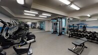 Located at 1022 S Oxford Ave in Los Angeles, this single-floor fitness center is thoughtfully designed to accommodate a wide range of training styles and fitness goals. The space is organized into distinct functional zones, each outfitted with purpose-driven equipment and connected by durable gray rubber flooring suited for high-activity use.

The cardio area features a row of modern treadmills and elliptical machines equipped with digital displays, positioned along a wall-length mirror that enhances the sense of openness throughout the space. Overhead, bright fluorescent lighting ensures consistent, even illumination across the entire floor.

The strength training section includes a multi-function cable machine, a power rack with a adjustable bench, and a full dumbbell rack offering a comprehensive range of weights. Additional functional training equipment includes kettlebells in varying sizes, medicine balls, stability balls, and foam exercise mats neatly organized on dedicated racks.

A standout design element is the serene, large-scale mountain landscape mural that runs along multiple walls, creating a calming visual backdrop throughout the space. Full-length mirrors amplify the room and support proper form during exercise. The overall atmosphere is clean, modern, and practical, offering a focused environment well-suited for diverse fitness routines.