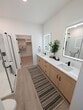 This 1,180 sq ft single-story home at 25 Cenote Cir in St. Augustine, FL offers a thoughtfully designed layout with 2 bedrooms and 2 bathrooms. The open-concept kitchen and living area is a standout, featuring two-tone cabinetry with warm natural wood lower cabinets and crisp white uppers, quartz countertops, stainless steel appliances, a kitchen island, and stylish pendant lighting. A distinctive barn-style sliding door adds a modern farmhouse touch. Light wood-look flooring runs throughout the main living areas, complementing the home's clean, contemporary aesthetic. The spacious living room offers a ceiling fan and an exterior door with a large window, filling the space with natural light and outdoor views. The primary bedroom spans 150 sq ft with plush carpeting and a ceiling fan, and connects to a well-appointed ensuite bathroom featuring a glass-enclosed walk-in shower, warm wood vanity with black hardware, and direct access to a shelved walk-in closet. The second bedroom also features carpet flooring and ample natural light. The second bathroom includes a soaking tub, wood vanity, and light wood flooring. A dedicated laundry room houses a full-size washer and dryer. Black hardware and fixtures are used consistently throughout, creating a cohesive, modern design language.